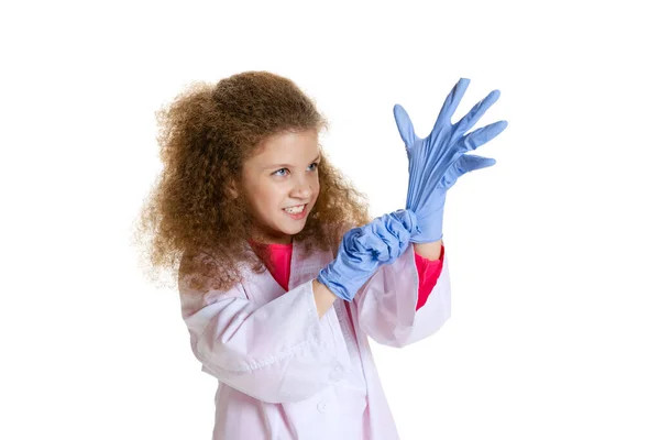 Half-length portrait of cute beautiful little girl, child in image of dentist doctor wearing white lab coat and gloves isolated on white studio background — стоковое фото
