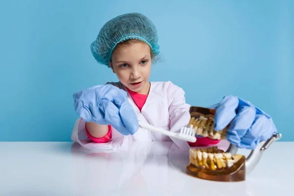 Συναισθηματικά χαριτωμένο κοριτσάκι, παιδί κατ 'εικόνα του οδοντιάτρου φορώντας λευκό εργαστηριακό παλτό και γάντια που απομονώνονται σε μπλε φόντο στούντιο — Φωτογραφία Αρχείου