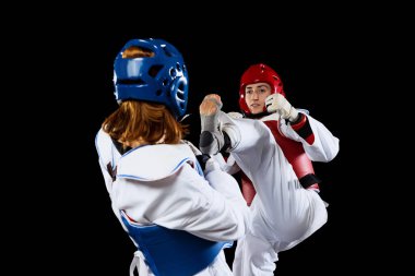 Close-up two young women, taekwondo athletes training together isolated over dark background. Concept of sport, skills