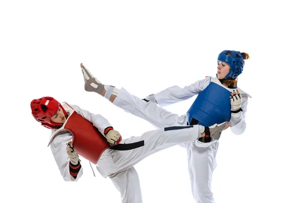 Dynamic portrait of two young women, taekwondo athletes training together isolated over white background. Concept of sport, skills — Stok fotoğraf