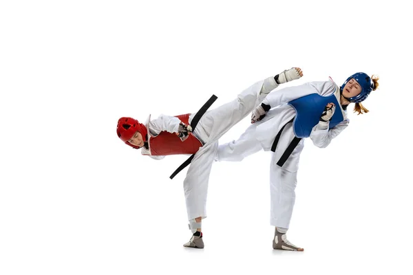 Dynamic portrait of two young women, taekwondo practitioners training together isolated over white background. Concept of sport, skills — стоковое фото