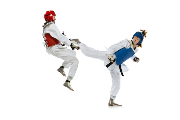 Dynamic portrait of two young women, taekwondo practitioners training together isolated over white background. Concept of sport, skills — Stockfoto