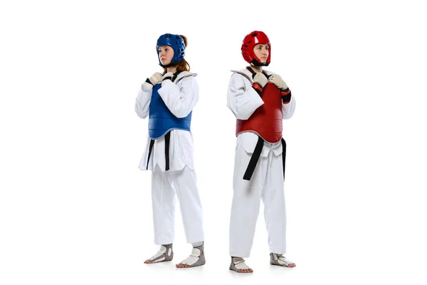 Studio shot of of two young women, taekwondo athletes practicing together isolated over white background. Concept of sport, skills — Foto de Stock
