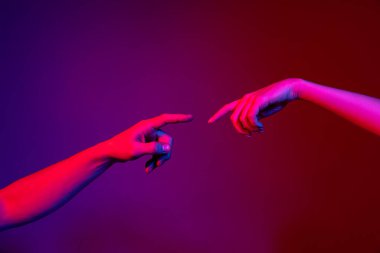 İki insan eli birbirine dokunmaya çalışıyor. Mor arka planda, neon ışıkta izole edilmiş. İnsan ilişkileri, toplum, birliktelik, sembolizm, kültür ve tarih kavramı