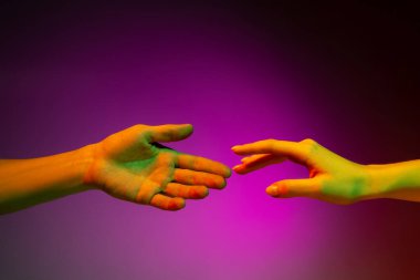 İki insan eli birbirine dokunmaya çalışıyor. Mor stüdyo arka planında, neon ışıkta izole edilmiş. İnsan ilişkileri, toplum, birliktelik kavramı