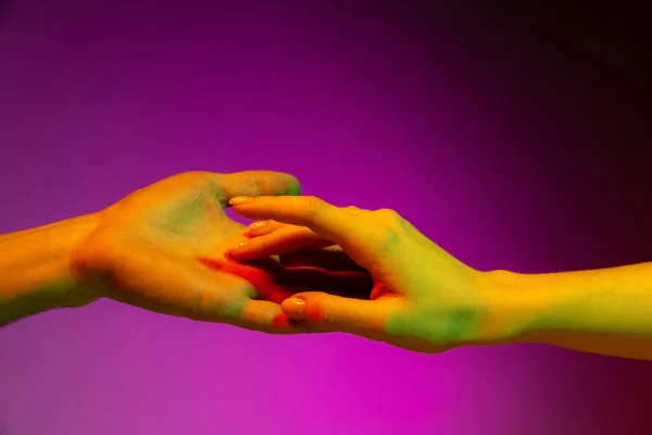 Две человеческие руки, пытающиеся прикоснуться друг к другу изолированы на фиолетовом фоне студии в неоновом свете. Понятие человеческих отношений, общности, единства — стоковое фото