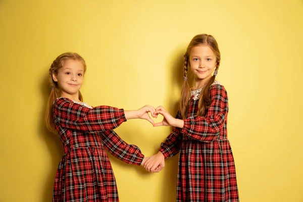 Портрет двох маленьких красивих дівчат, братів і сестер у плетених сукнях ізольовані на жовтому тлі. Поняття дитинства, емоції — стокове фото
