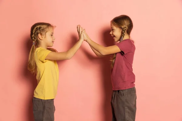 Веселі маленькі дівчата, сестри або брати і сестри носять повсякденний одяг, який грає ізольовано на рожевому тлі. Поняття дитинства, емоції — стокове фото