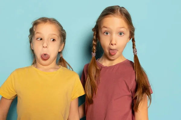 Студійний знімок милих маленьких дівчат, сестер або братів і сестер у повсякденному одязі, ізольованому на синьому фоні. Поняття дитинства, емоції — стокове фото