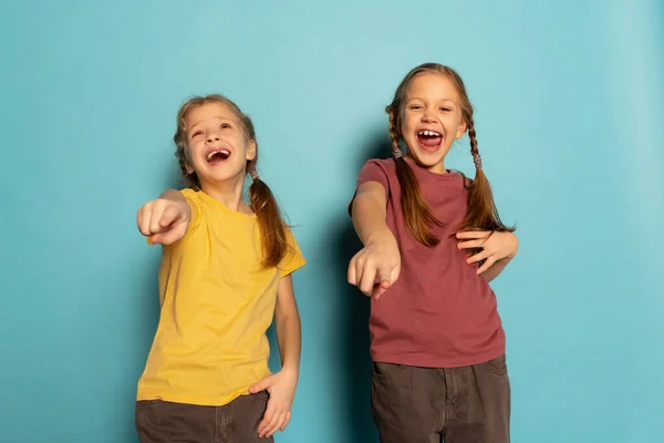 Щасливі маленькі дівчата, сестри або брати і сестри в повсякденному одязі сміються ізольовано на синьому фоні. Поняття дитинства, емоції — стокове фото