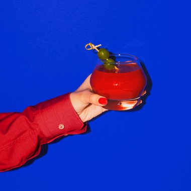 Parlak mavi neon arka planda izole edilmiş kokteylli kadın el kamerası. Zevk anlayışı, alkollü içkiler