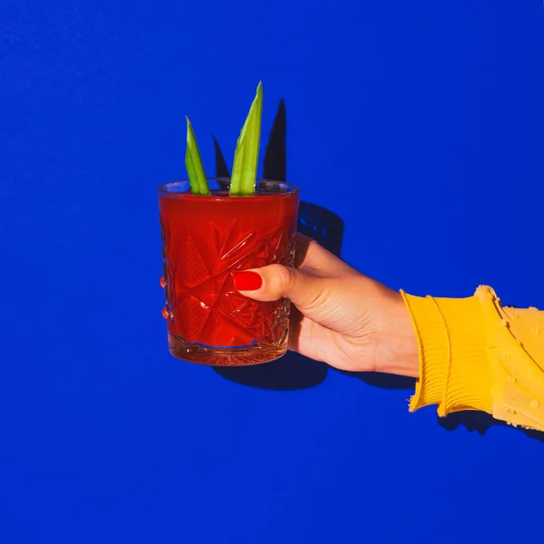 Женская рука держит стакан с коктейлем, изолированным на ярко-голубом неоновом фоне. Концепция вкуса, алкогольные напитки — стоковое фото