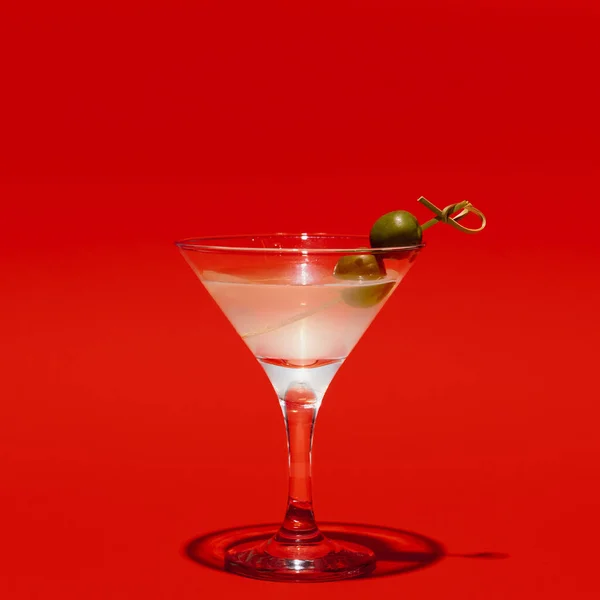 Martini-Glas mit Oliven isoliert auf leuchtend rotem Neonhintergrund mit Schatten. Geschmackskonzept, alkoholische Getränke — Stockfoto