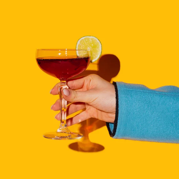 在明亮的黄色霓虹灯背景上隔离的雌性手握玻璃杯。品味的概念，酒精饮料 — 图库照片