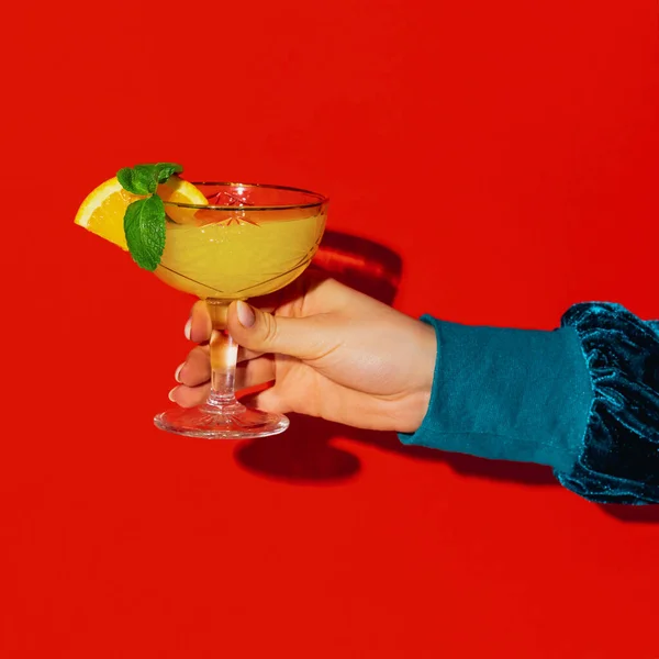 Weibliche Hand hält Glas mit Schraubendreher-Cocktail isoliert auf leuchtend rotem Neonhintergrund. Geschmackskonzept, alkoholische Getränke — Stockfoto