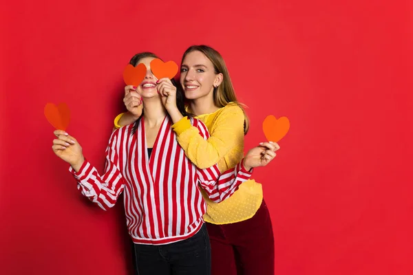 Retrato de duas jovens meninas felizes isoladas em fundo vermelho. Celebração do dia dos namorados. Conceito de emoções, amor, relações, férias românticas. — Fotografia de Stock