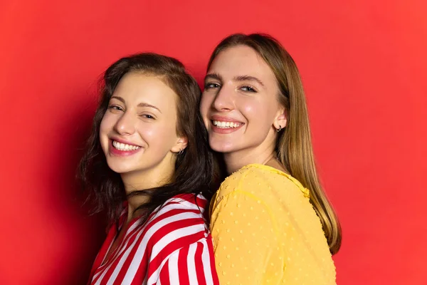Retrato de meia-duração de duas jovens meninas felizes isoladas em fundo vermelho. Celebração do dia dos namorados. Conceito de emoções, amor, relações, férias românticas. — Fotografia de Stock