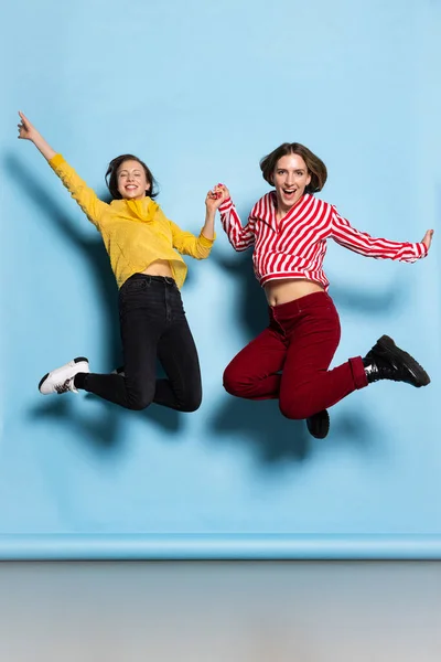 Estúdio tiro de meninas jovens emocionais, casal pulando isolado em fundo azul. Dia dos Namorados celebração. — Fotografia de Stock