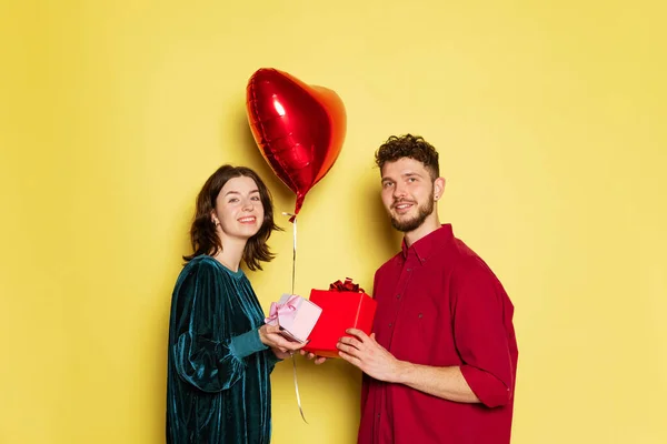 Pareja feliz, hombre y mujer sosteniendo globos en forma de corazones y caja de regalo. Celebración de San Valentín. Concepto de emociones, amor, relaciones, vacaciones románticas. — Foto de Stock