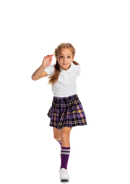 Portrait of cute little girl, pupil in school uniform running isolated on white background. Concept of childhood, emotions, study — Stock Photo, Image