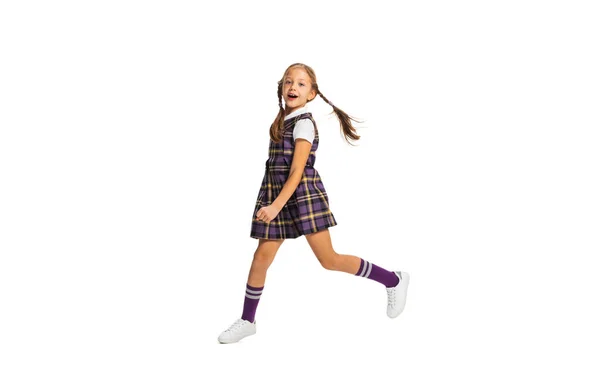 Ritratto di bambina carina, pupilla in uniforme scolastica che corre isolata su sfondo bianco. Concetto di infanzia, emozioni, studio — Foto Stock