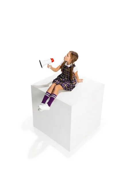 Студия снимает красивую маленькую девочку, ученицу в школьной форме, сидящую на большом ящике изолированном на белом фоне. Концепция детства, эмоции, учеба — стоковое фото