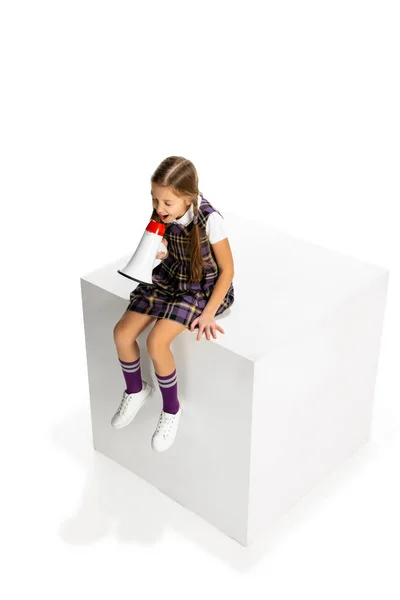 Щаслива красива дівчинка, учень у шкільній формі сидить на великій коробці і кричить на мегафоні ізольовано на білому тлі . — стокове фото