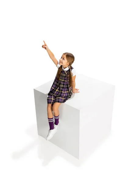 Студійний знімок красивої маленької дівчинки, учень у шкільній формі сидить на великій коробці ізольовано на білому тлі. Концепція дитинства, емоцій, навчання — стокове фото
