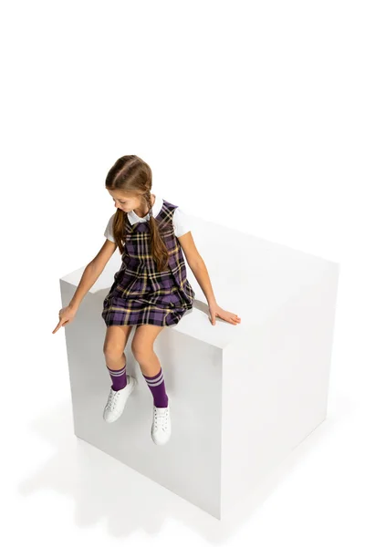 Студійний знімок красивої маленької дівчинки, учень у шкільній формі сидить на великій коробці ізольовано на білому тлі. Концепція дитинства, емоцій, навчання — стокове фото