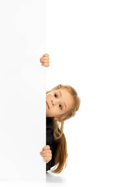 Vtipné dítě, holčička, žák v neformálním stylu, který vykukuje zpoza zdi izolované na bílém pozadí. Pojem dětství, emoce, studium — Stock fotografie