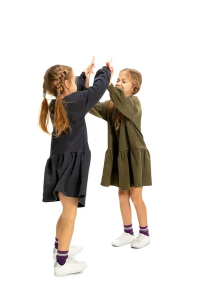 Веселі маленькі дівчата, сестри або брати і сестри носять повсякденний одяг у стилі, який грає ізольовано на білому фоні студії. Концепція дитинства, емоцій, навчання — стокове фото