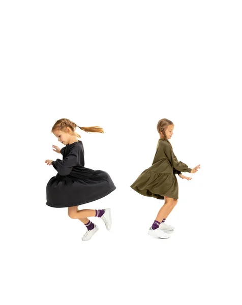 Симпатичні маленькі дівчата, сестри або брати і сестри в повсякденному одязі, танцюють ізольовано на білому фоні студії. Концепція дитинства, емоцій, навчання — стокове фото