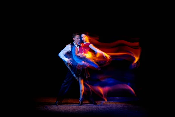 Retrato dinámico de jóvenes bailarines de salón bailando tango argentino aislado sobre fondo oscuro con luz mixta de neón. — Foto de Stock