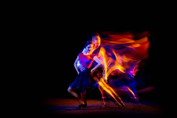 Portrait dynamique de jeunes danseurs de salon dansant le tango argentin isolé sur fond sombre avec néon lumière mixte. — Photo