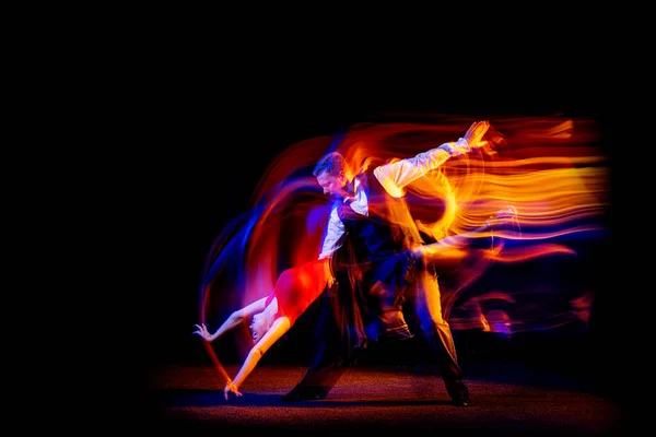 Retrato dinámico de jóvenes bailarines de salón bailando tango argentino aislado sobre fondo oscuro con luz mixta de neón. — Foto de Stock