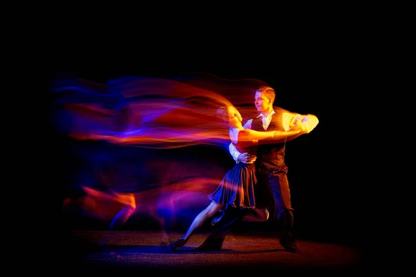 Dynamisch portret van jonge ballroom dansers dansen Argentijnse tango geïsoleerd op donkere achtergrond met neon gemengd licht. — Stockfoto