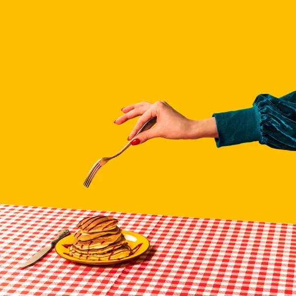 Étel pop art fotózás. Női kéz és édes palacsinta a kockás asztalterítőn, élénk sárga háttérrel. Szüreti, retro stílus — Stock Fotó