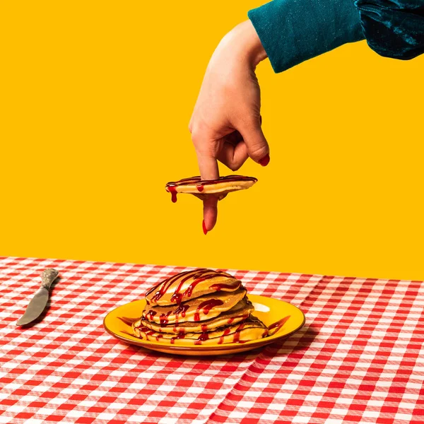 푸드 팝 아트 사진. 밝은 노란색 배경에서 분리 된 누르스름 한 식탁보 위에 있는 암컷 손 과 달콤 한 팬케이크. 고전적 이고, 원곡적 인 — 스톡 사진