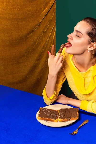 Fotografía de arte pop de comida. Chica joven degustación de tostadas de chocolate dulce aislado sobre vintage, interior de estilo retro. Concepto de comida, creatividad. — Foto de Stock