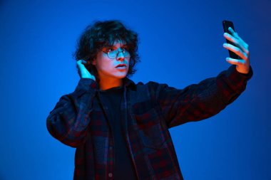 Siyah kapüşonlu bir öğrenci, koyu mavi arka planda izole edilmiş bir telefon kullanıyor. Duyguların kavramı