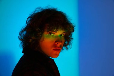 Üzgün adamın yakın çekimi, öğrenci mavi arka planda izole edilmiş kameraya bakıyor neon ışıkta. Duyguların kavramı, öğrenim, eğitim, moda