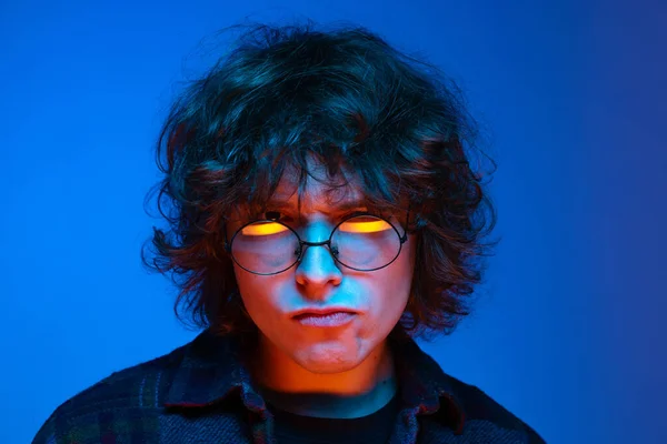 Cara de primer plano del hombre triste, estudiante mirando a la cámara aislada sobre fondo azul en luz de neón. Concepto de emociones, estudio, educación, moda —  Fotos de Stock