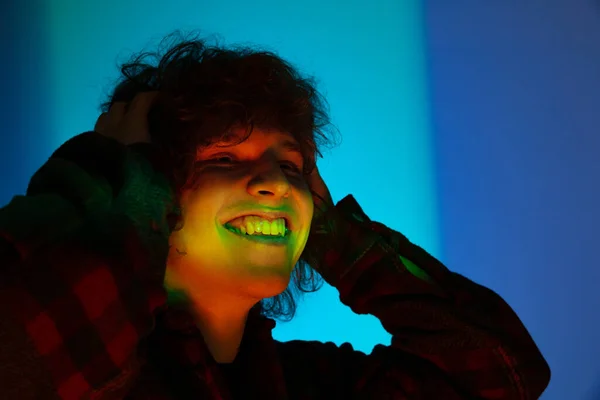 Porträt eines jungen lächelnden Mannes, Student in schwarzem Kapuzenpulli isoliert auf dunkelblauem Hintergrund in Neonlicht. Konzept von Emotionen, Mimik, Jugend, Sehnsucht, Verkauf — Stockfoto