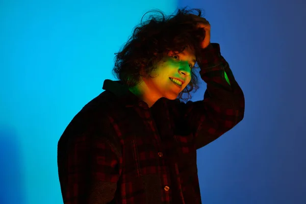 Porträt eines jungen lächelnden Mannes, Student in schwarzem Kapuzenpulli isoliert auf dunkelblauem Hintergrund in Neonlicht. Konzept von Emotionen, Mimik, Jugend, Sehnsucht, Verkauf — Stockfoto