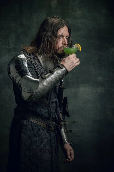 Portrét středověkého válečníka nebo rytíře se špinavou zraněnou tváří držícího koktejlové sklo izolované nad tmavým pozadím. Porovnání období, historie — Stock fotografie