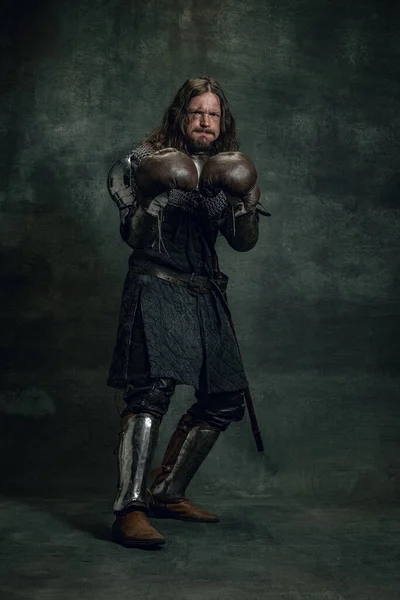 Πορτρέτο του μεσαιωνικού πολεμιστή ή ιππότη με βρώμικα τραυματισμένα γάντια πυγμαχίας πρόσωπο απομονώνονται σε σκοτεινό φόντο. Σύγκριση εποχών, ιστορία — Φωτογραφία Αρχείου