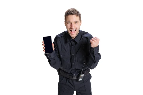 Portret młodego człowieka, policjant w czarnym mundurze z telefonem odizolowanym na białym tle. Pojęcie pracy, kariery, prawa i porządku. — Zdjęcie stockowe