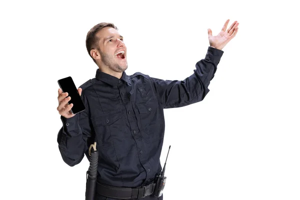 Portrait of young excited man, policeman officer wearing black uniform using phone isolated on white background. Concept of job, caree, law and order. — Stock Photo, Image