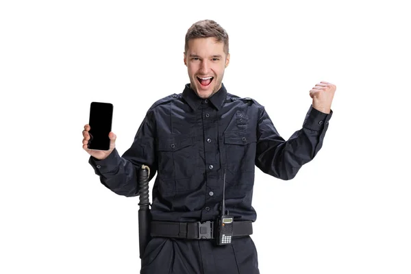 Портрет молодого человека, офицера полиции в черной униформе с использованием телефона, изолированного на белом фоне. Концепция работы, кари, правопорядка. — стоковое фото