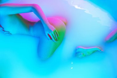 Süt banyosunda yumuşak pembe neon parıltısıyla uzanan zayıf genç kızın en iyi görüntüsü. Güzellik, moda, tarz, vücut bakımı, kaplıca konsepti.